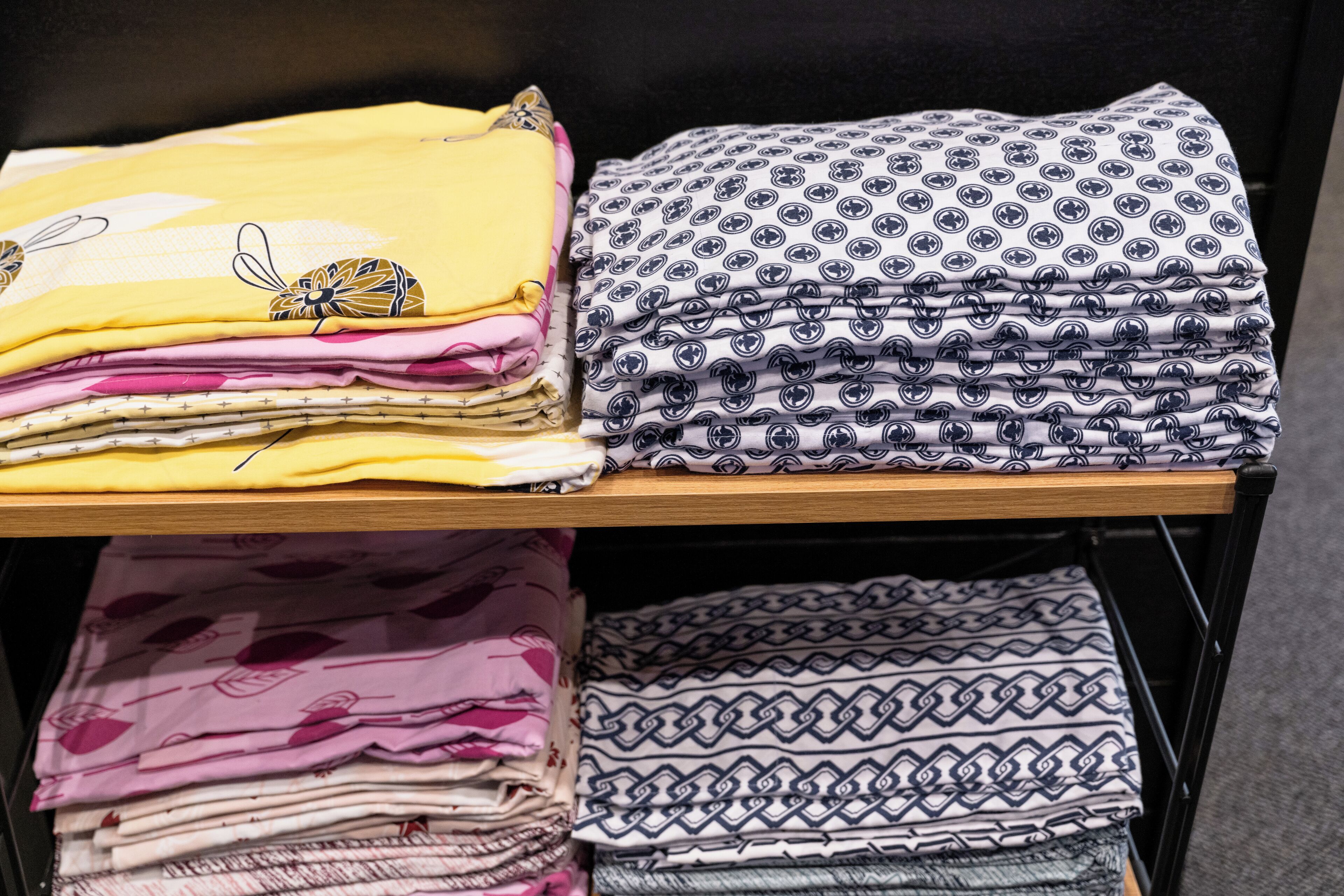 A stack of folded blankets with various patterns and colors on a shelf.