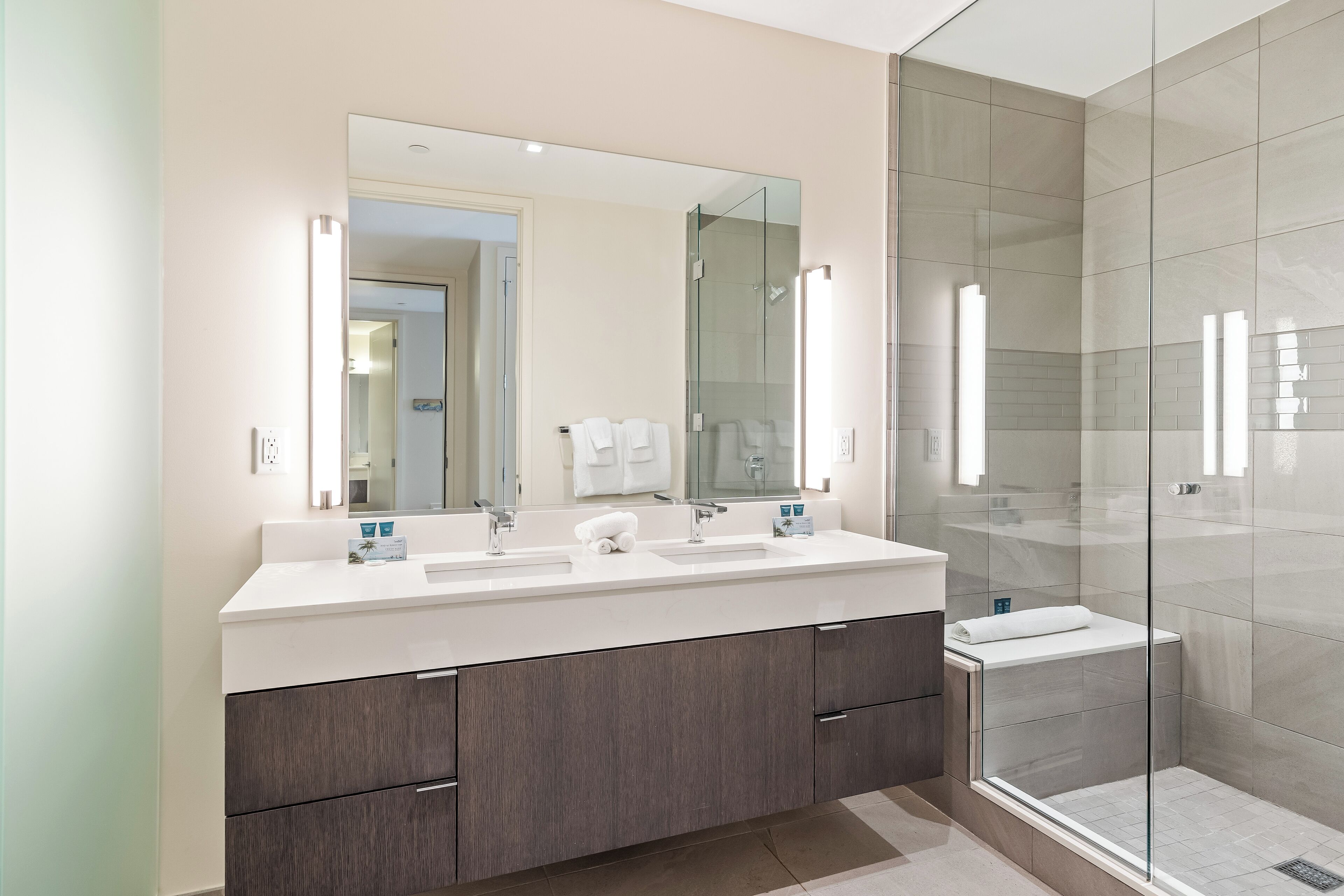 A modern bathroom with a large mirror, two sinks, and a glass-enclosed shower.