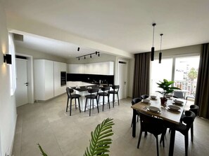 Une cuisine moderne avec des meubles blancs, un îlot central doté de chaises et un coin repas avec une table dressée pour quatre personnes.