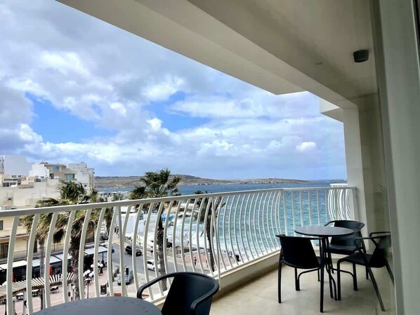 A balcony with a view of the sea, a table with chairs, and a railing.