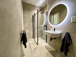 A modern bathroom with a glass shower enclosure, a sink, and a large mirror.