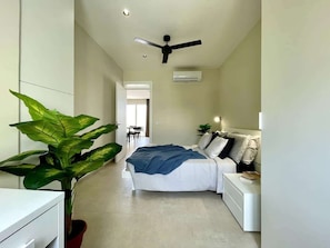 Une chambre à coucher comprenant un lit, des tables de chevet, un ventilateur de plafond, un appareil de climatisation et une plante en pot.