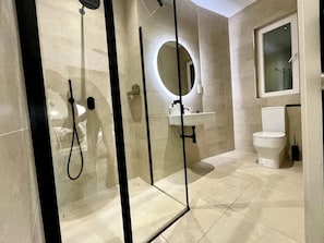 Une salle de bain moderne avec une douche à parois de verre, un miroir rond, des toilettes et un lavabo.