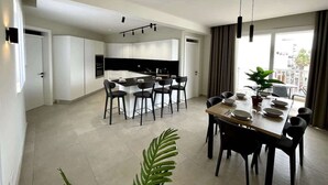 Una cocina moderna con armarios blancos, una isla central con sillas y un comedor con una mesa dispuesta para cuatro.