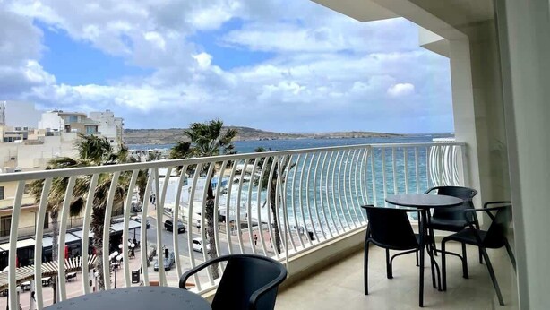 Un balcón con vista al mar, una mesa con sillas y una barandilla.