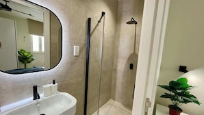 A bathroom with a white sink, a mirror, a shower enclosure, and a potted plant. - FL10 2BR Bugibba Seafront LUX Apartment (Saint Paul's Bay)