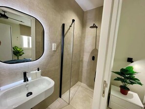 Une salle de bain avec un lavabo blanc, un miroir, une cabine de douche et une plante en pot.