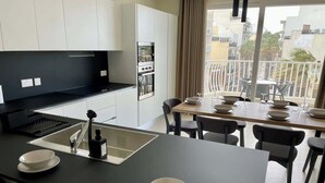 A modern kitchen with white cabinets, a black countertop, and a dining area with a table and chairs. - FL10 2BR Bugibba Seafront LUX Apartment (Saint Paul's Bay)