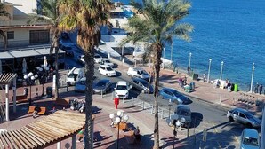 A coastal area with parked cars, palm trees, and a view of the sea. - FL10 2BR Bugibba Seafront LUX Apartment (Saint Paul's Bay)