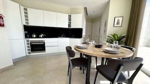 A modern kitchen with white cabinets, a built-in oven, and a dining area with a round table and four chairs.