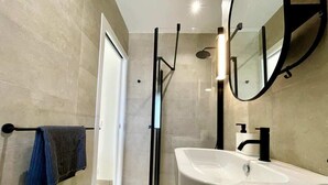 A modern bathroom with a white sink, a towel rack with towels, a shower area, and a mirror.
