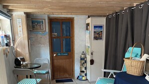 A cozy room with a wooden door labeled "MA Chambre," a small table with a radio, a chair with a striped cushion, a blue tablecloth with a nautical theme, and a wicker basket. - 100m from the beach! (Hermanville-sur-Mer)