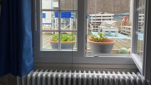 A room with a large window overlooking a backyard with a pool, outdoor furniture, and potted plants. - 100m from the beach! (Hermanville-sur-Mer)