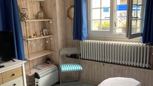 A cozy bedroom with a bed, a chair, a radiator, and shelves against the wall. - 100m from the beach! (Hermanville-sur-Mer)