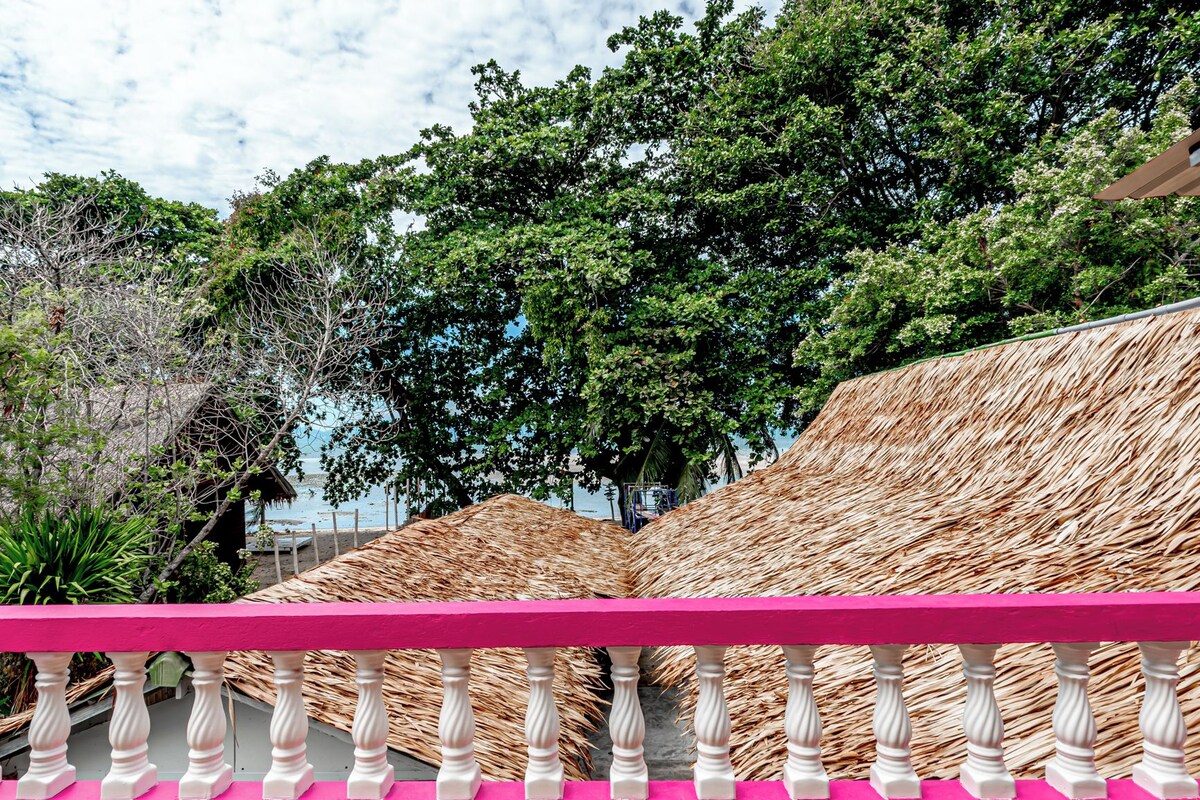 A beachside view with thatched umbrellas and a pink railing.