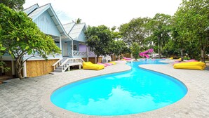 A swimming pool with a slide, surrounded by trees and a building with a blue facade. - Slumber Party Koh Phangan Beach (Ko Pha-ngan)