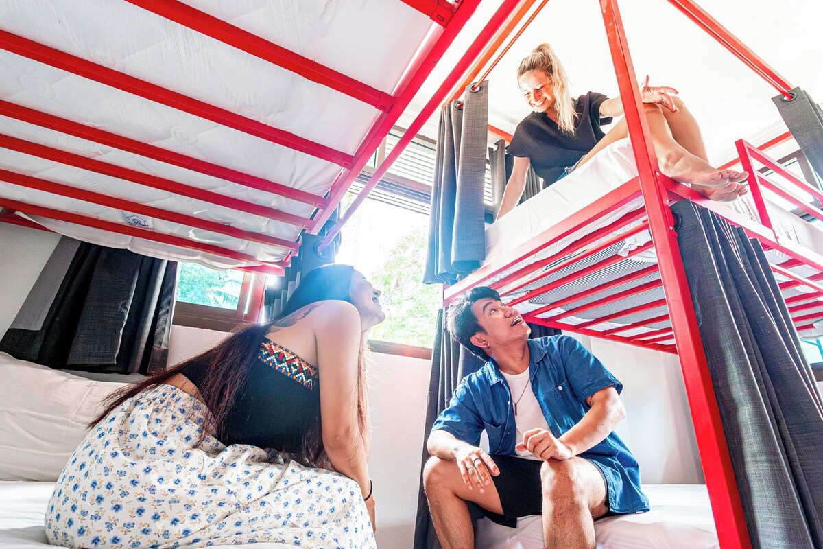 A room with a bunk bed, a window with curtains, and a bed with a floral-patterned cover.