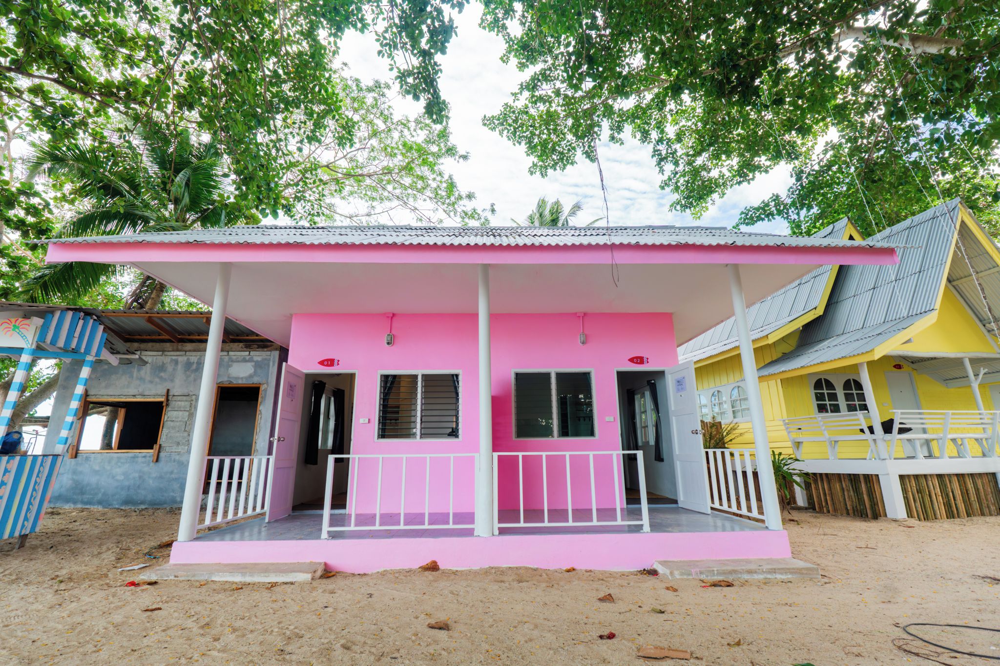 A pink building with a white porch and a yellow building adjacent to it.