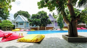 Un espace piscine avec une piscine à l’eau d’un bleu limpide, des chaises longues et un arbre.