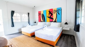A hotel room with two beds, a large colorful artwork on the wall, a window with curtains, and a small table with a lamp. - Slumber Party Koh Phangan Beach (Ko Pha-ngan)