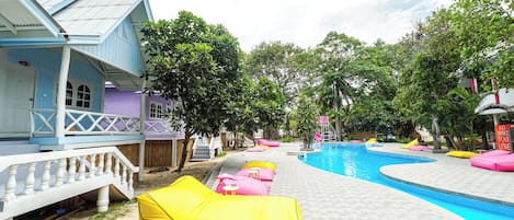 Un área de piscina con sillas de descanso de colores y una piscina azul cristalina.