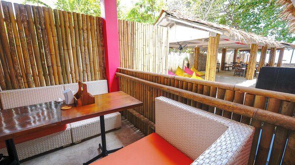 Un área de estar al aire libre con paredes de bambú, muebles de mimbre y una estructura de techo de paja.