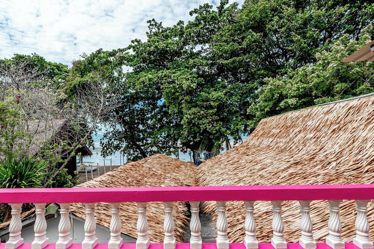 Une vue sur la plage, avec des parasols en chaume et une balustrade rose.