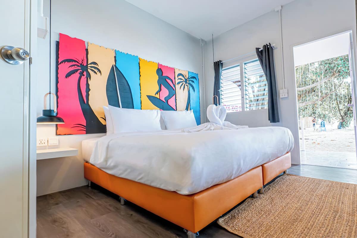 Une chambre à coucher comprenant un lit, une table de chevet, une œuvre d’art murale, une fenêtre avec des rideaux et une vue sur l’extérieur.