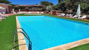 Une piscine rectangulaire à l’eau d’un bleu limpide, entourée d’une pelouse bien entretenue et de chaises longues blanches.