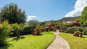 A stone pathway leading to a building surrounded by lush greenery and red flowering plants.