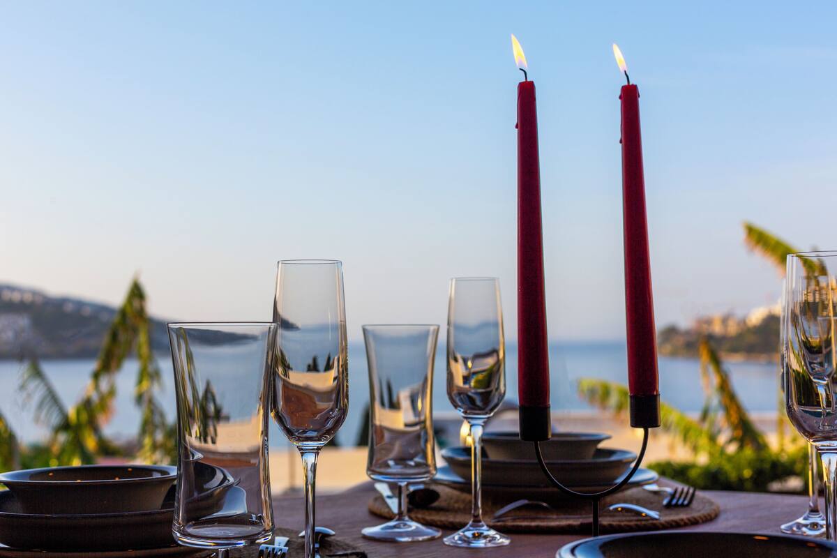 A table set for a meal with glasses and plates, candles, and a view of the sea.
