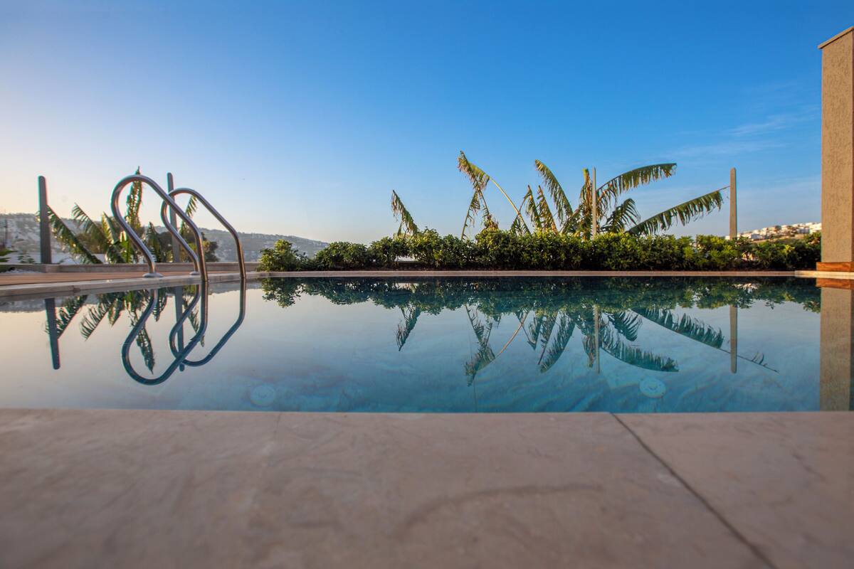 A swimming pool with clear water reflecting palm trees and a metal sculpture.