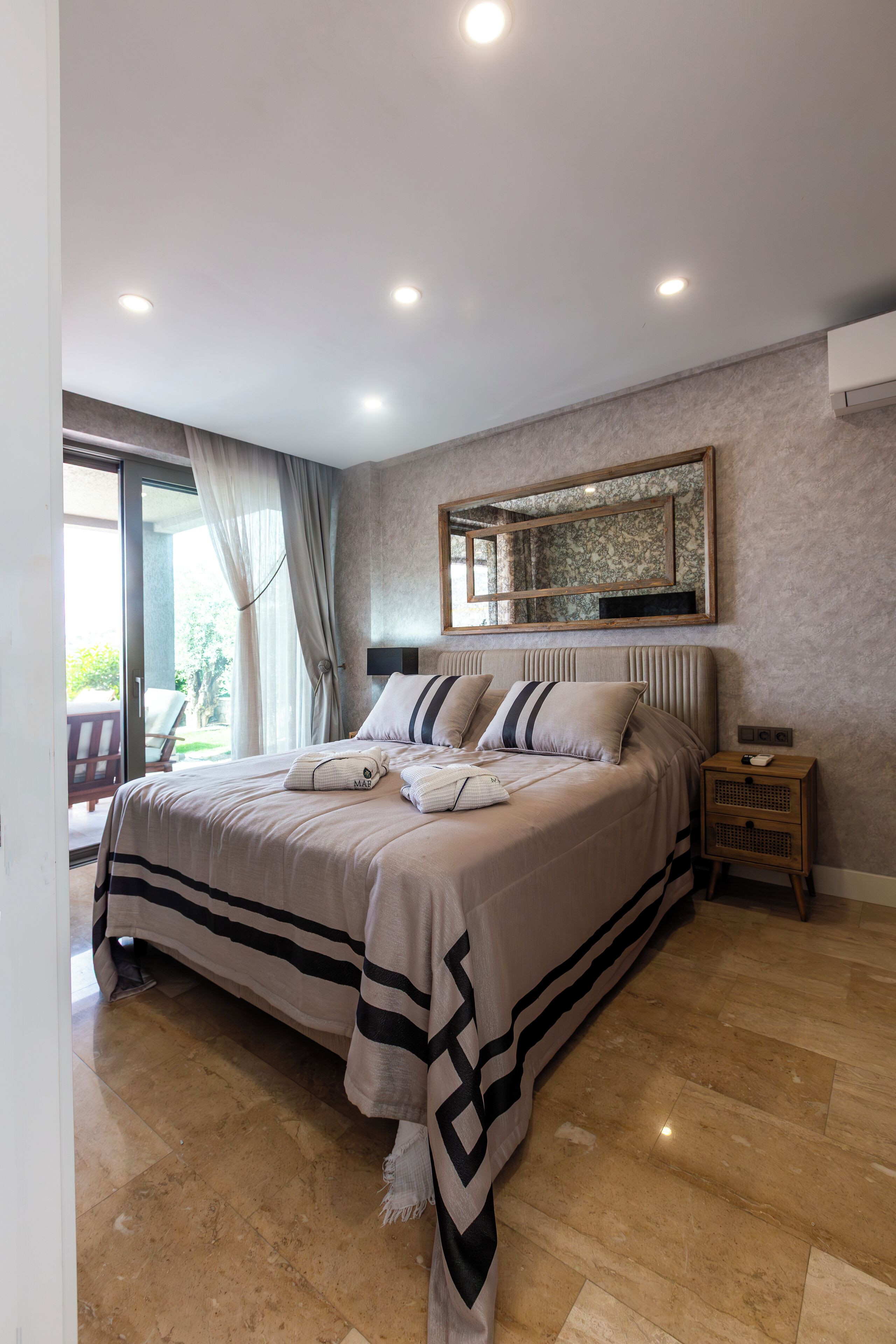 Un dormitorio con una cama grande, una mesita de noche, un espejo y vistas al exterior.