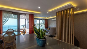A modern hotel room with a dining area, a sofa, and a large window with a view of the sea. - Marje Villas Bodrum (Bodrum)