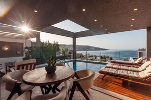 A modern outdoor pool area with a view of the sea, a wooden table with chairs, and lounge chairs. - Marje Villas Bodrum (Bodrum)