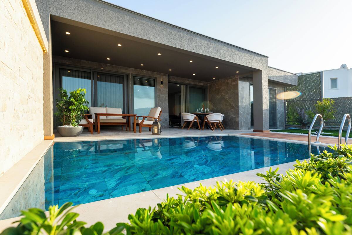 A modern outdoor pool area with a built-in seating area, a table, and potted plants.