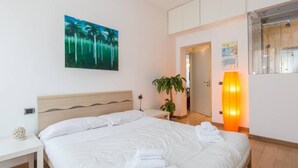 A hotel room with a bed, a bedside table, a wall-mounted painting, a potted plant, and a lit lamp. - Testaccio Elegant Apartment (Rome)