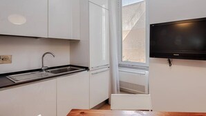 A compact kitchen with white cabinets, a black countertop, a built-in sink, a window, and a mounted television. - Testaccio Elegant Apartment (Rome)