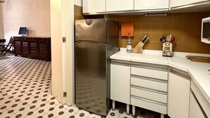 Una cocina compacta con un refrigerador de acero inoxidable, armarios blancos, un microondas y un piso estampado.