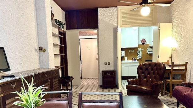 Comedor con una mesa de madera, sillas, una planta en maceta, un ventilador de techo y una cocina al fondo.