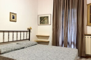A bedroom with a bed, a headboard, two framed pictures, a window with curtains, and a radiator. - P031 - Porto Recanati, three-room apartment with terrace 100m from the sea (Porto Recanati)