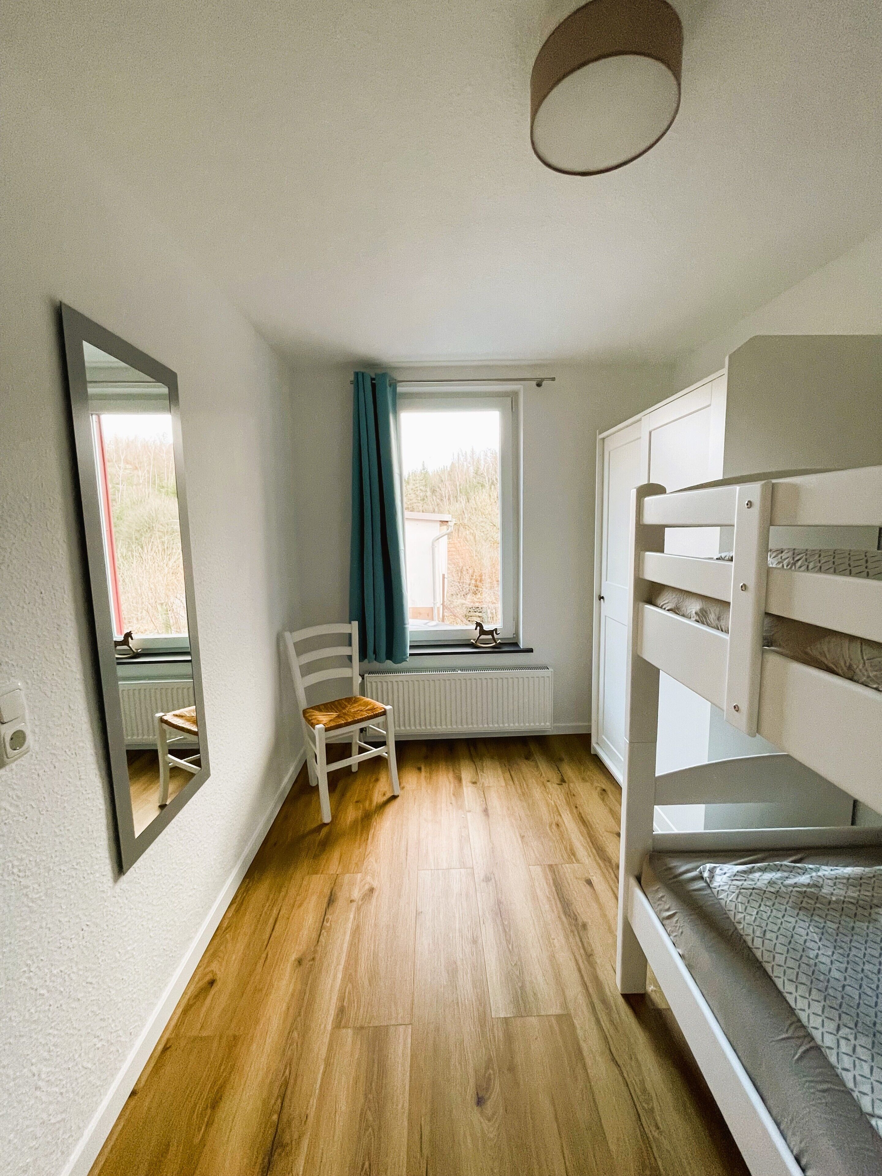 Ein Zimmer mit einem Etagenbett, einem Sessel, einem Heizkörper und einem fenster mit Vorhängen.
