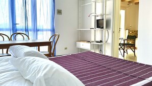 A bedroom with a bed, a desk, and a chair. There is a window with curtains, a TV on a shelf, and a door leading to another room. - Palme 10 - Marcelli, two-room apartment with garden, Residence Le Palme (Marcelli)