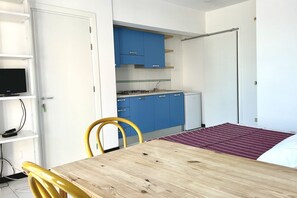Een kleine kamer met een houten tafel, een gele stoel, blauwe kastjes en een witte deur.