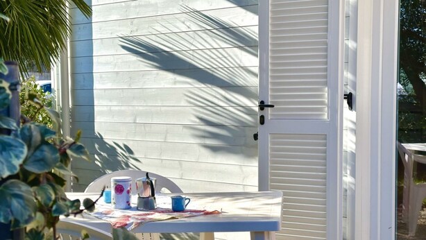 A white table with a blue mug and a white mug, a white chair, and a closed white door. - Palme 10 - Marcelli, two-room apartment with garden, Residence Le Palme (Marcelli)