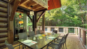 A wooden deck with a glass-top table set for dining, surrounded by wicker chairs, and overlooking a forested area. - At only 7 km from Mont-Tremblant Skiing,  Dream Chalet with Spa & Fireplace (Lac superieur)