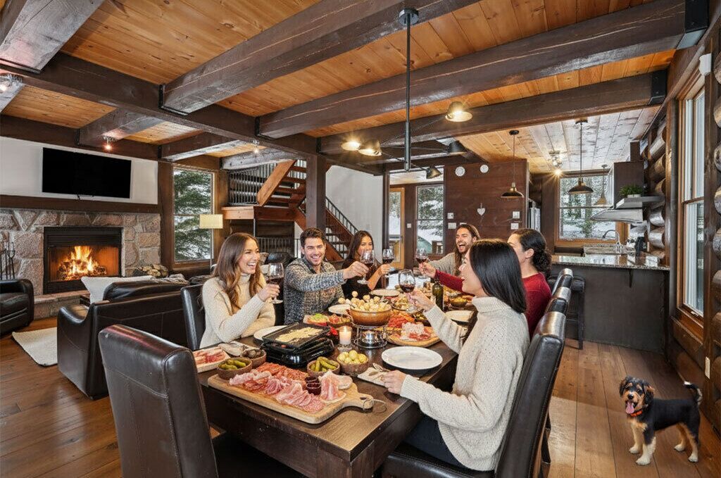 A cozy dining area with a stone fireplace, wooden beams, and a large window overlooking a snowy landscape.