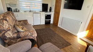 Ein kompakter Wohnbereich mit Sofa, Essbereich, einer Küche mit Geräte und einem an der Wand befestigten Fernseher.