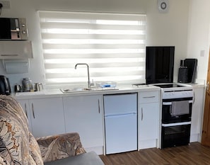 A compact kitchen with a built-in oven, a dishwasher, and a window with blinds.