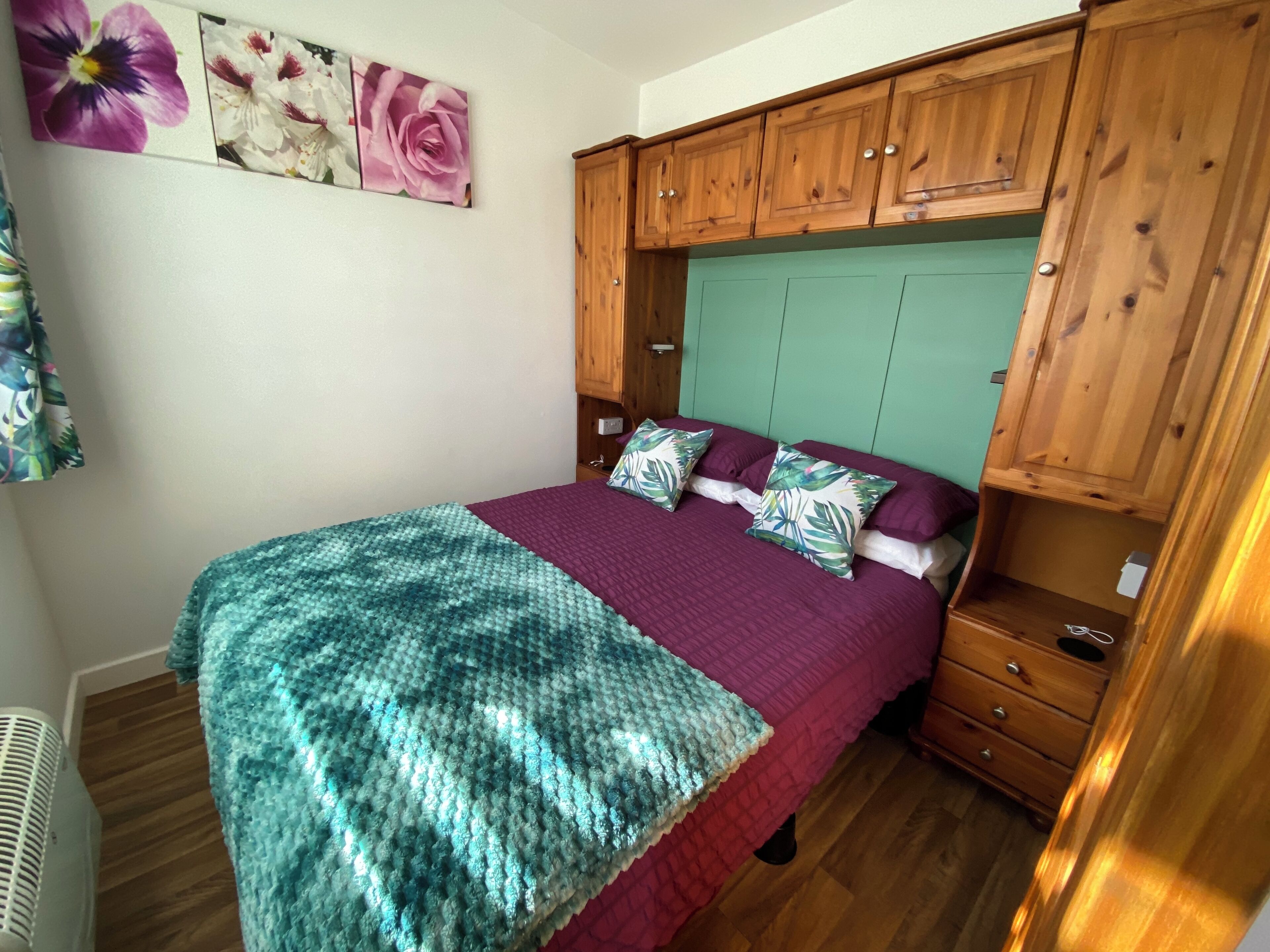 A bedroom with a bed, a wooden wardrobe, a green headboard, and a floral artwork on the wall.
